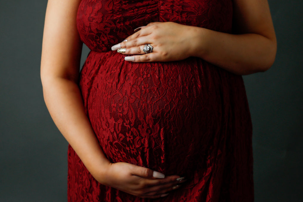 Up close of baby bump in red dress by Olivia Acton Photography located in Janesville, WI
