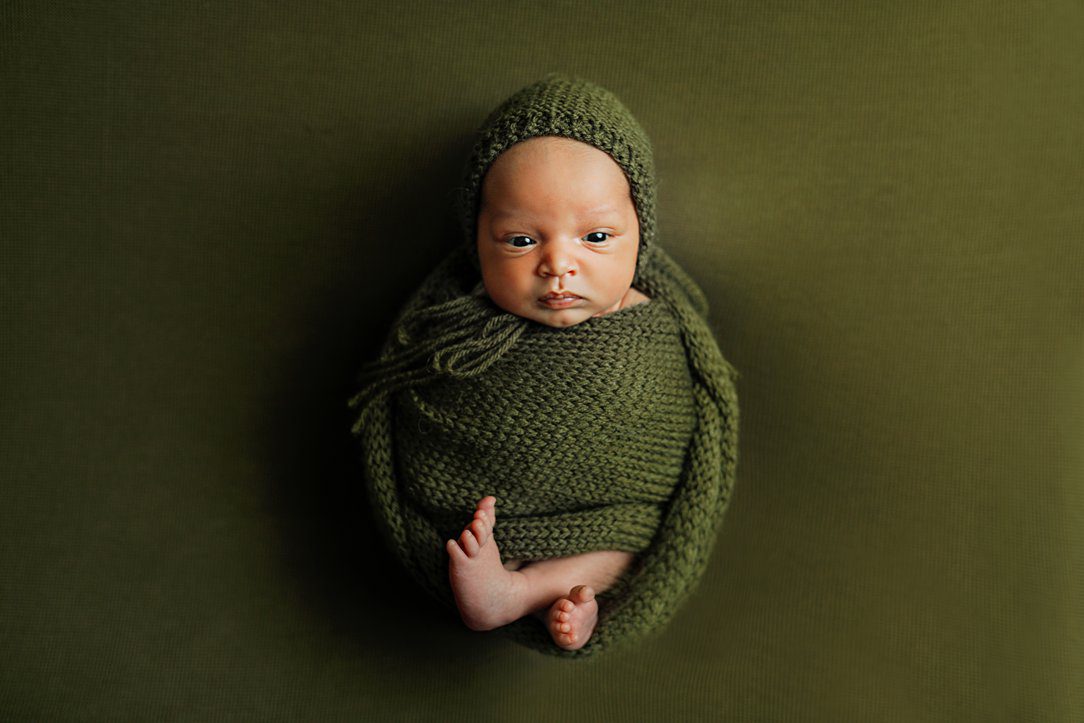 Newborn boy in green wrap with bonnet during newborn session by Olivia Acton