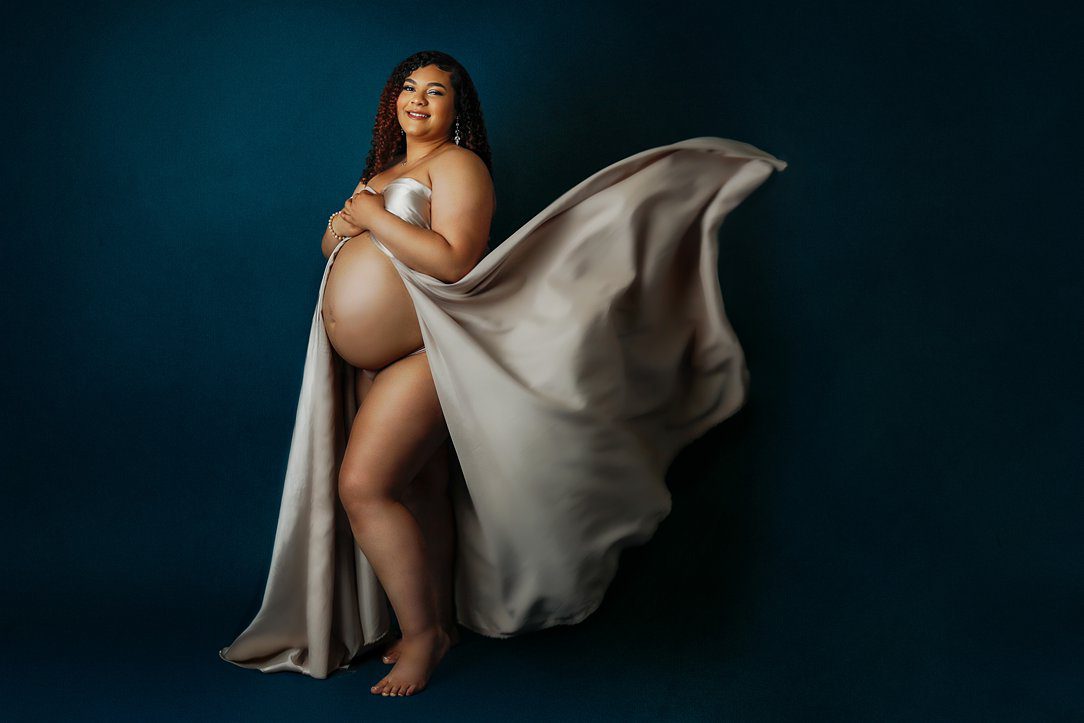 Mom in fabric during maternity session in studio against blue background in Janesville, WI