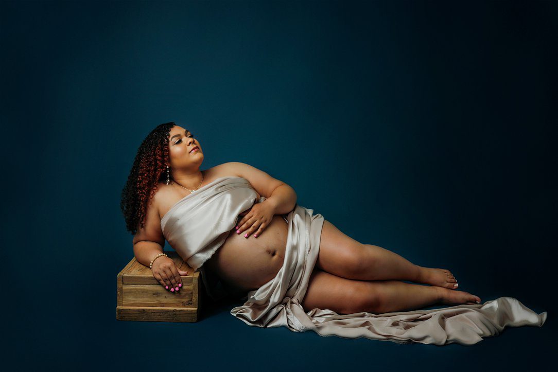 Momma lying down pose for maternity session in studio against blue background by Olivia Acton Photography