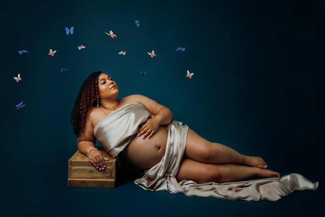 Momma lying down pose for maternity session in studio against blue background in Janesville, WI