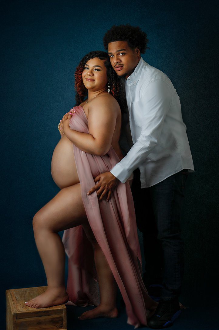 Couples maternity session in studio against blue background in Janesville, WI