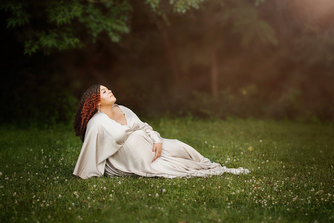 Pregnant mother sitting at maternity session holding hands outdoors in Janesville, WI by Olivia Acton